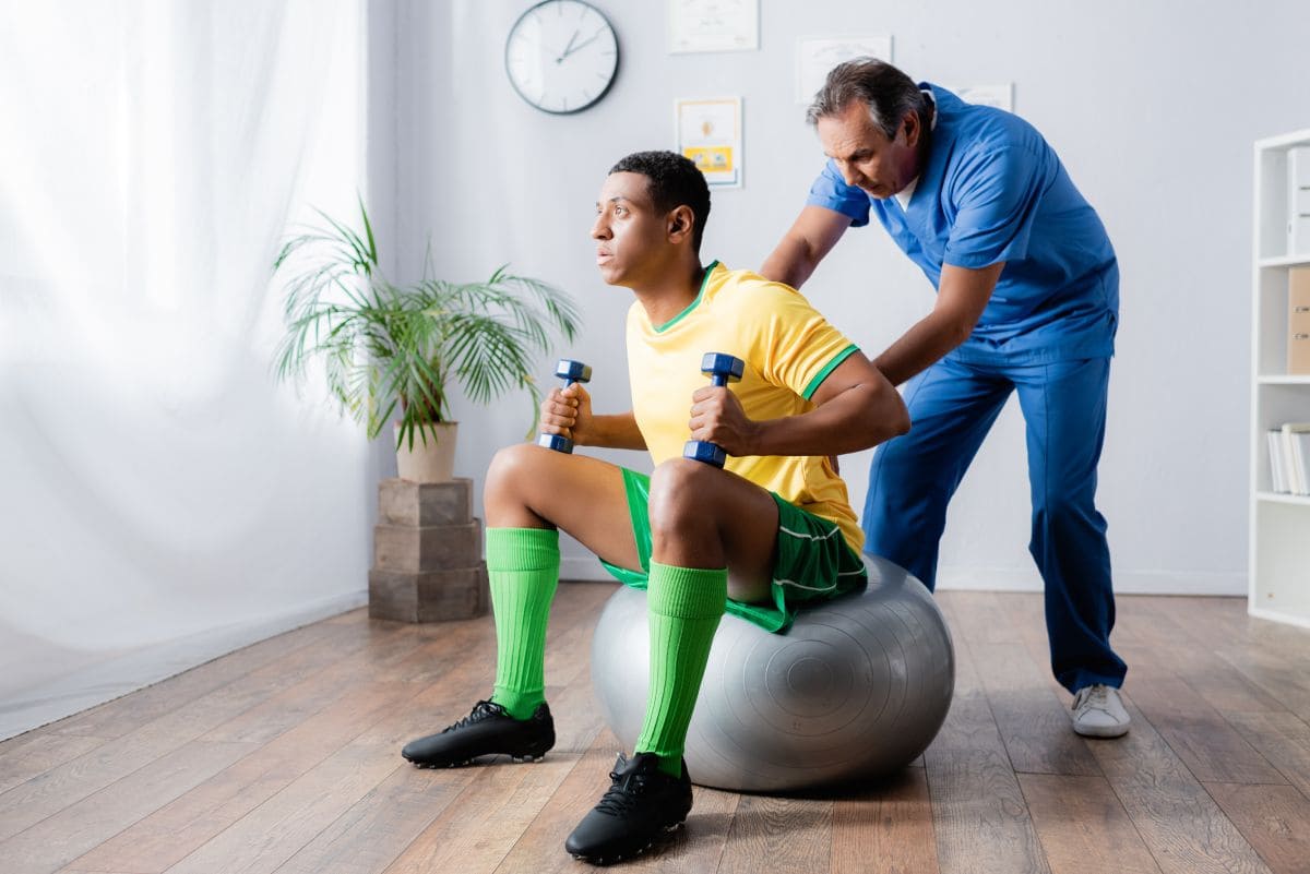 Young adult practicing a standing balance activity with a therapist nearby